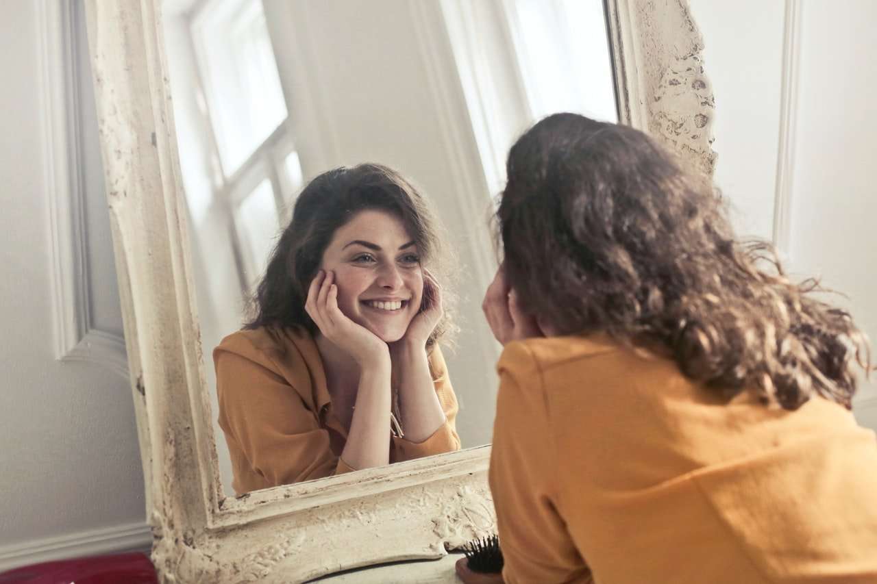 women smiling at her lip lines in the mirror